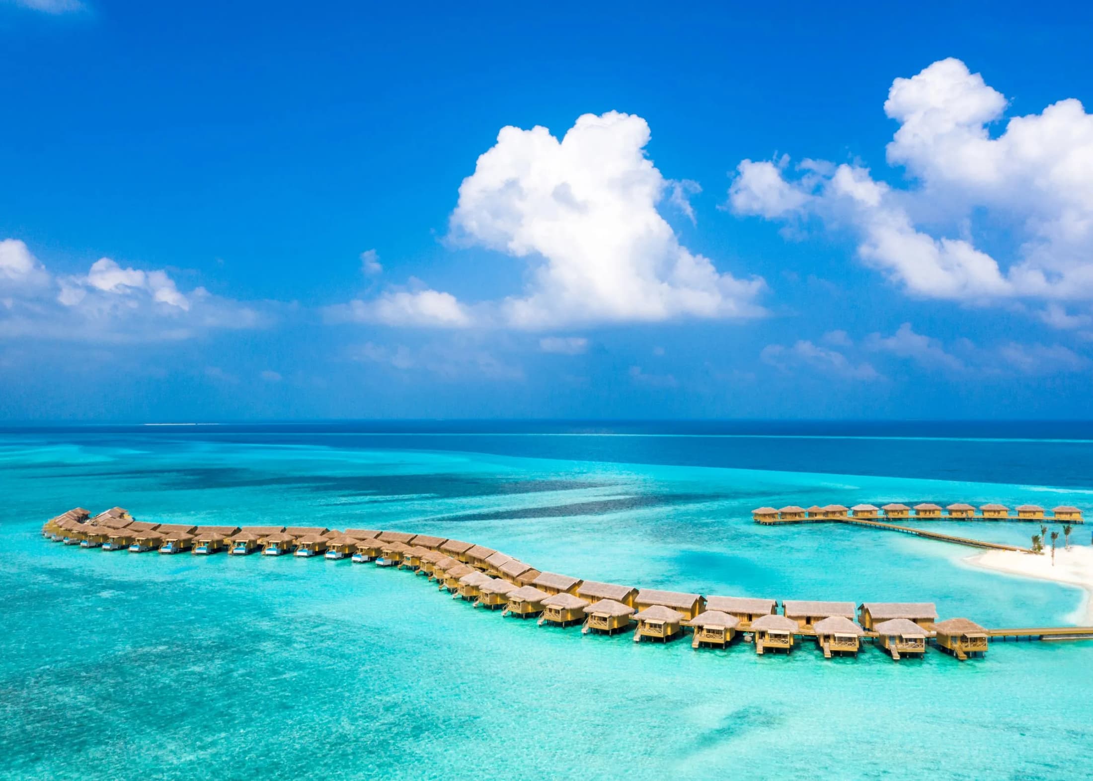 A long line of overwater villas stretching into the Maldives lagoon, seen from above