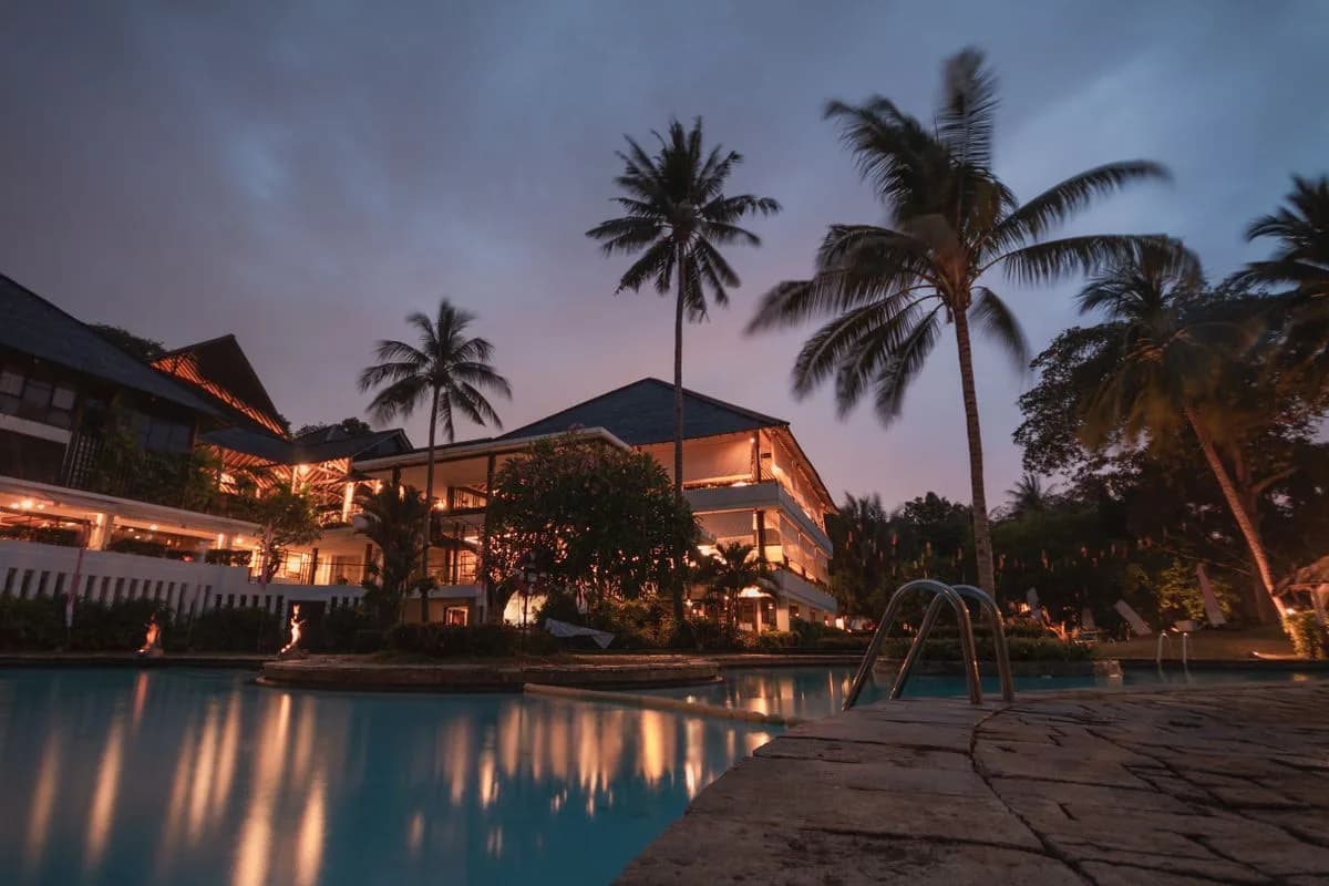 A resort pool lit at night beneath tall palms