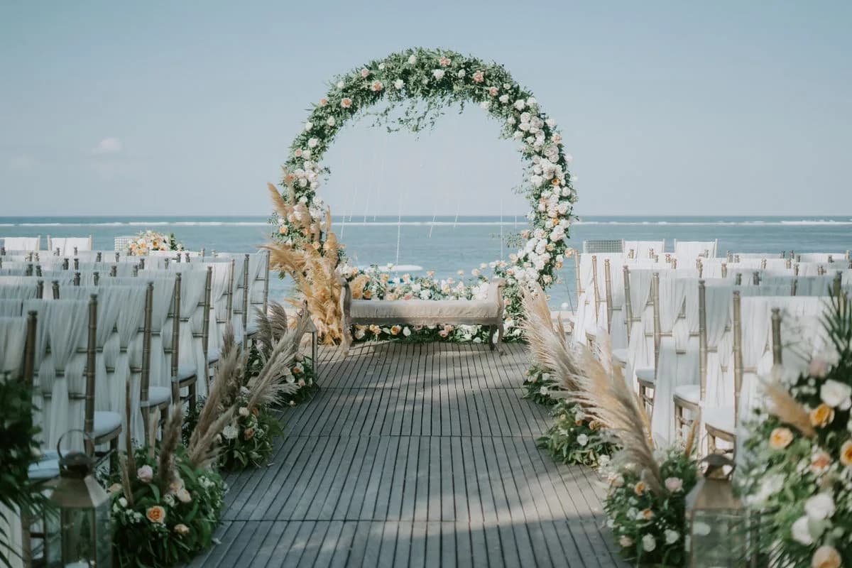 A floral ceremony arch on a deck above the sea