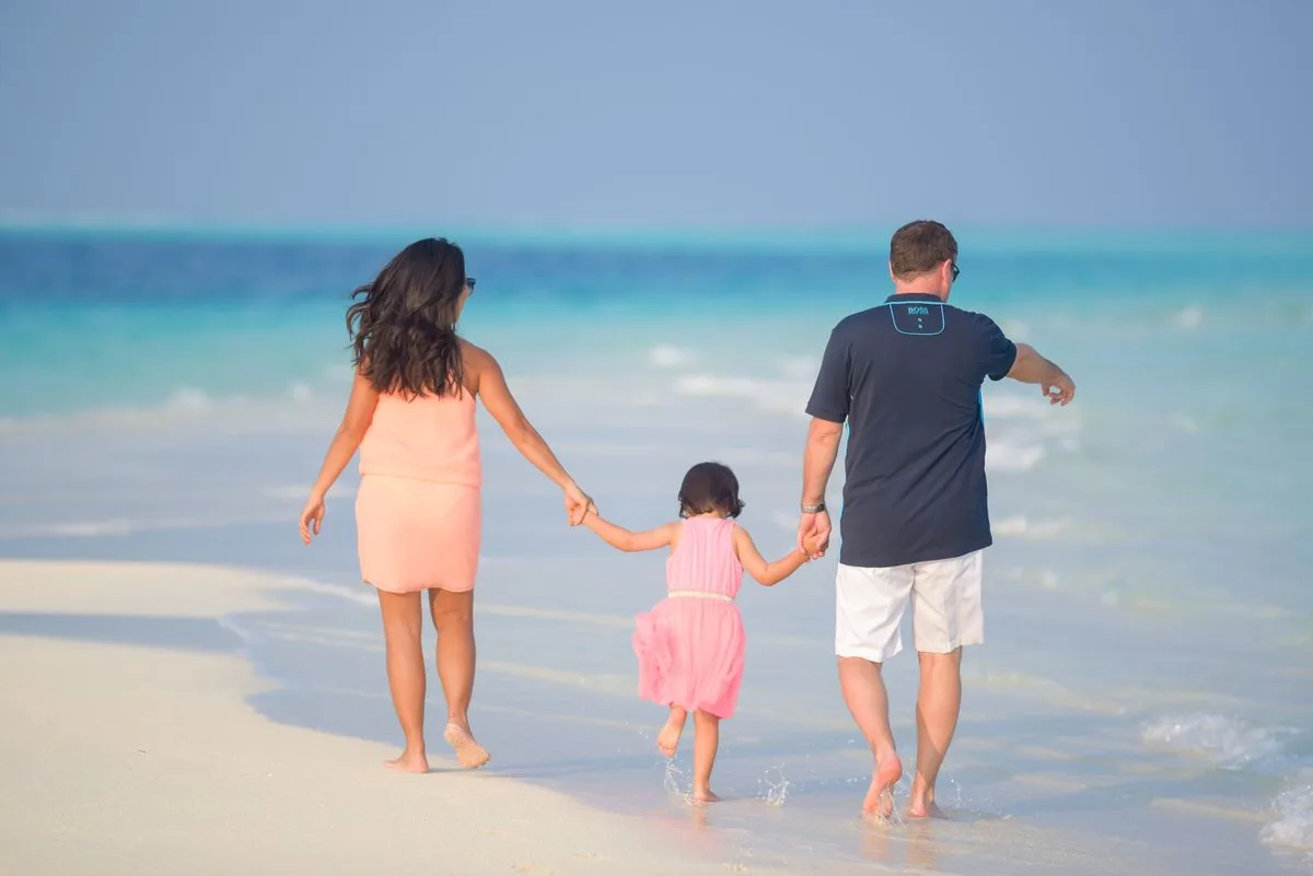 A family walking hand in hand along a white-sand beach